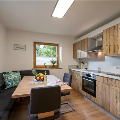 A modern kitchen with wooden furniture and a large window front. Fresh fruit is on the table, and there is an inviting bench.