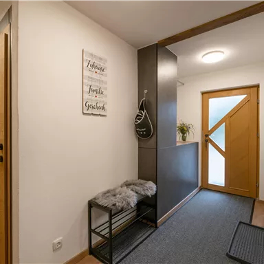 A modern hallway with wooden doors and a bright entrance door. A small table with a cloth and a plant creates an inviting atmosphere.