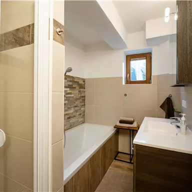 A modern bathroom with a shower and a bathtub. It has elegant tiles and wood elements for a warm, inviting look.