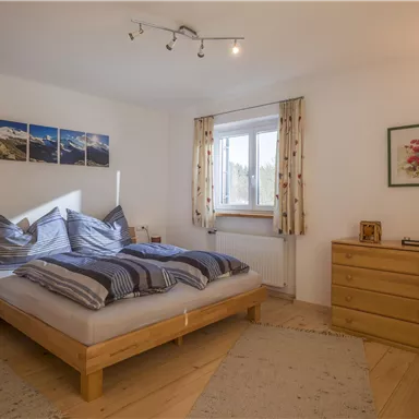 Ein gemütliches Schlafzimmer mit einem großen Bett und blau-gestreiften Bettdecken. Die Wände sind hell, und es gibt ein Fenster mit Vorhängen sowie einige dekorative Bilder.