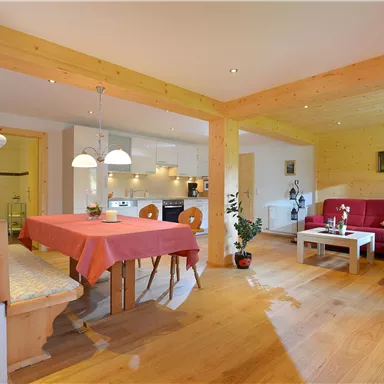 Ein gemütlicher Wohnraum mit einem Esstisch und einer roten Couch. Der Raum hat Holzböden und viel natürliches Licht.