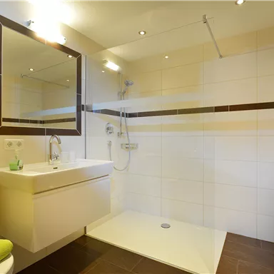 Ein modernes Badezimmer mit einer großen Dusche und einem eleganten Waschbecken. Die Wände sind hell gefliest, und frische Handtücher liegen bereit.