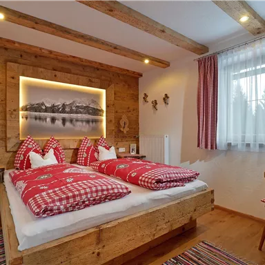 Ein gemütliches Schlafzimmer mit Holzdekor und zwei Betten. Die Bettwäsche ist rot kariert, und ein Fenster sorgt für viel Tageslicht.