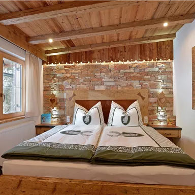 Ein gemütliches Schlafzimmer mit Holzdekor und einem Doppelbett. Die Wände sind mit Stein und warmem Licht gestaltet, und ein Fenster bietet einen Blick nach draußen.