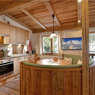 Eine moderne Küche mit Holzelementen und einem gemütlichen Essbereich. Große Fenster bieten Blick auf die Natur.