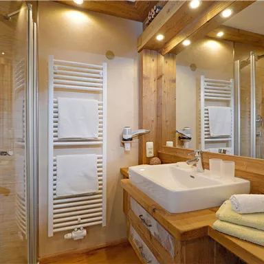 Ein modernes Badezimmer mit Holzverkleidung und eleganten Armaturen. Die Dusche ist glasüberdacht und es gibt frische Handtücher auf der Ablage.