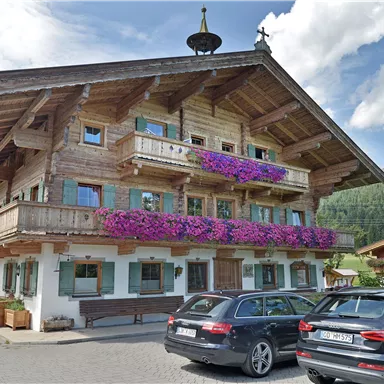 A traditional wooden house with colorful flower boxes. Parked cars in front of the picturesque mountain landscape.