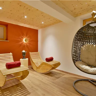 A relaxing space with two wooden lounge chairs and a hanging wicker chair. The walls are in warm colors, creating a cozy atmosphere.