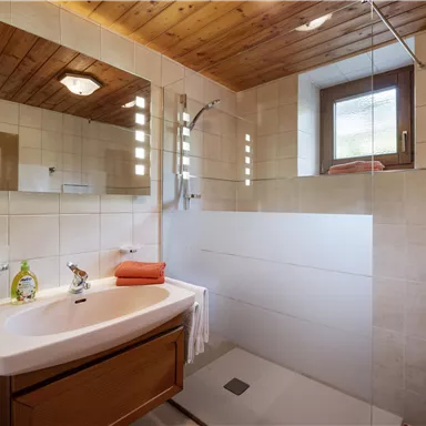 Ein modernes Badezimmer mit einer Dusche und einem vaskularen Waschbecken. Holzverkleidung an der Decke und große Fliesen sorgen für ein gemütliches Ambiente.