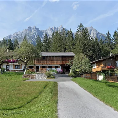 A picturesque landscape with traditional chalets and green meadows. In the background, majestic mountains rise under a clear sky.