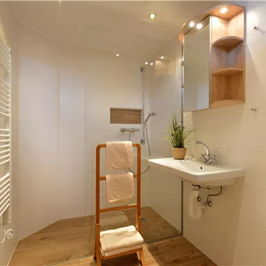 Ein modernes Badezimmer mit Dusche und einem kleinen Waschbecken. Holzdetails und Pflanzen sorgen für eine angenehme Atmosphäre.
