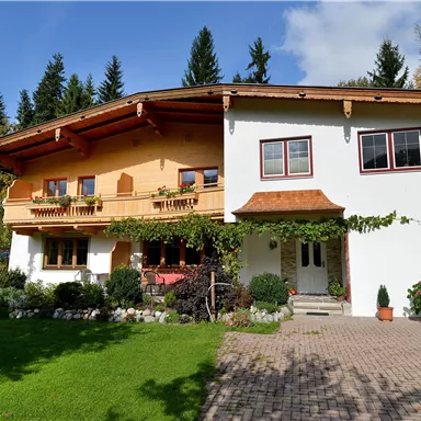 Ein schönes, traditionelles Haus mit einem Holz-Balkon und blühenden Pflanzen. Der Garten ist gepflegt und von Bäumen umgeben.