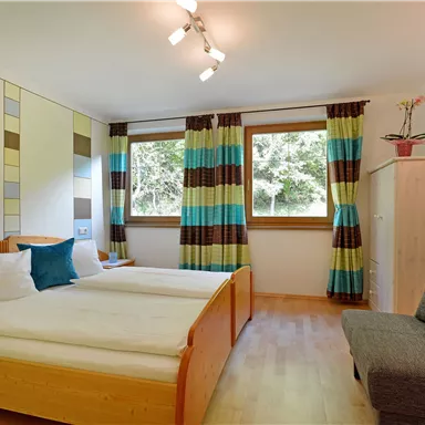 Ein gemütliches Schlafzimmer mit zwei Betten und modernen Möbeln. Große Fenster sorgen für viel Tageslicht und eine angenehme Atmosphäre.