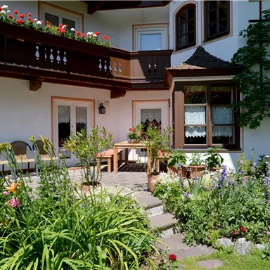 A beautiful courtyard with blooming plants and seating options. The building has a cozy charm with balconies and windows.
