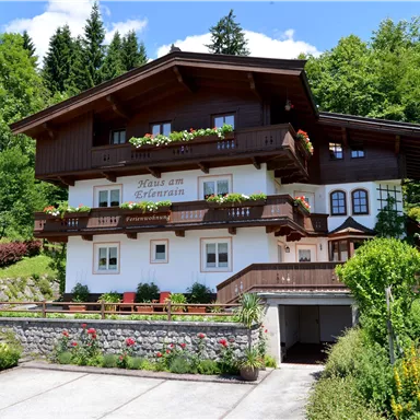 A lovely, traditional house in Alpine design with colorful flower balconies. Surrounded by green countryside and trees.