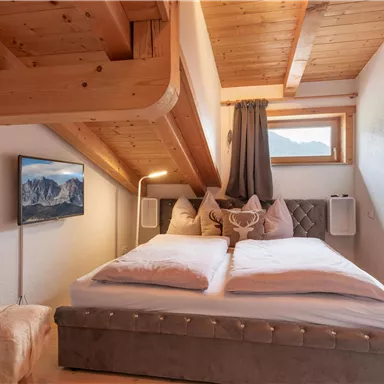 A cozy bedroom with a wooden ceiling and a view of the mountains. The bed is comfortable and modernly furnished.