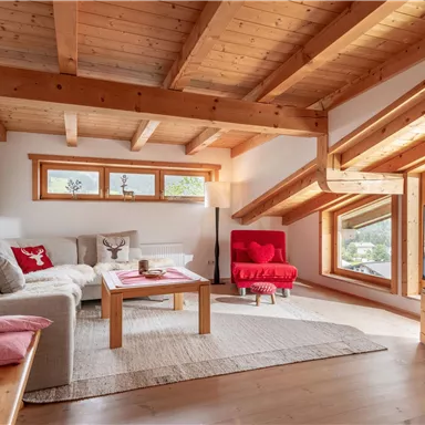 A bright living room with a wooden ceiling and large windows. There are comfortable furniture and a television that complements the space.