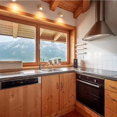 A cozy wooden kitchen with modern appliances. It offers a beautiful view of the mountains through large windows.