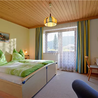 Ein gemütliches Schlafzimmer mit zwei Betten und bunten Kissen. Der Raum hat einen großen Fenster mit schöner Aussicht und einen Fernseher.