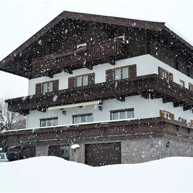 Ein charmantes Haus im Schnee mit mehreren Balkonen. Der Schnee fällt sanft und bedeckt die Landschaft.