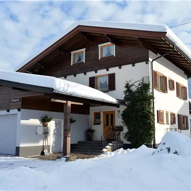 A beautiful two-story house with a gabled roof, surrounded by snow. The sky is clear with some clouds.