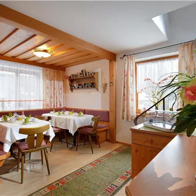 A cozy dining area with wooden decor and windows that let in plenty of light. Fresh flowers are on the tables, and the tables are set for guests.