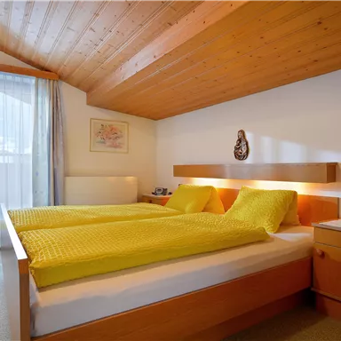 A cozy bedroom with a double bed and bright yellow bedspreads. Large windows provide plenty of daylight and a relaxed atmosphere.