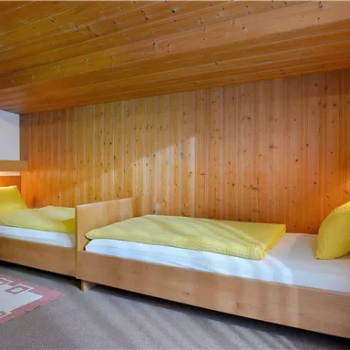 A cozy bedroom with two single beds and wood paneling. On the nightstand is a small flower in a pot.