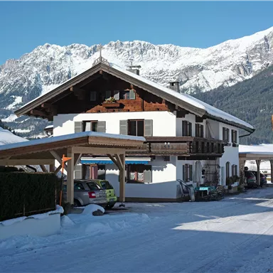 Ein charmantes Haus in den Alpen, umgeben von schneebedeckten Bergen. Der klare blaue Himmel ergänzt die winterliche Landschaft.