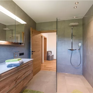 A modern bathroom with a glass shower and a beautiful wooden washbasin. The walls are in neutral gray tones, giving the space an elegant atmosphere.