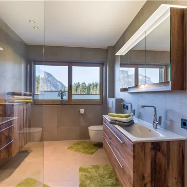 A modern bathroom with wooden details and large windows. The view of nature creates a bright and friendly atmosphere.