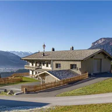 A modern house in the mountains with a beautiful view of the landscape. The surroundings are green and the mountains are visible in the background.