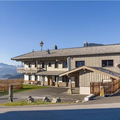 A modern building in the mountains with a clear blue sky.  
Surrounded by a beautiful landscape and a wooden plank.