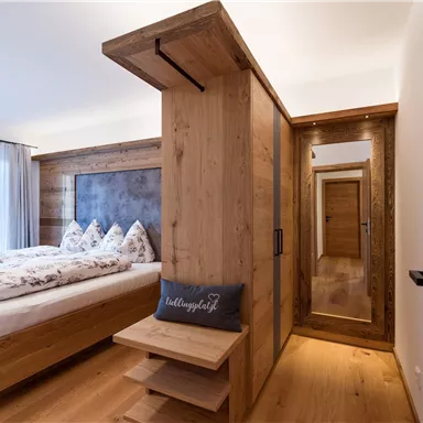 A modern bedroom with wood paneling and a large bed. Large windows let in plenty of light and offer a view outside.