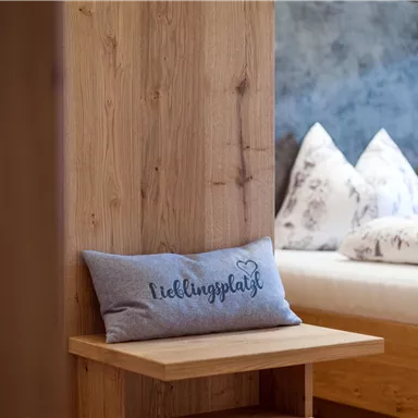 A cozy bedroom with a wooden design. A cushion with the print "Favorite Spot" lies on a bench.