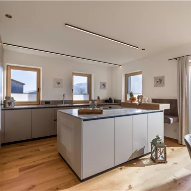 A modern kitchen with a large island and plenty of natural light. The wooden floors and the windows create an inviting atmosphere.