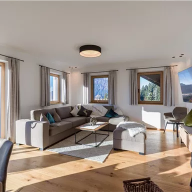 A modern living room with cozy furniture and large windows offering a view of the mountains. The room has a bright and inviting character.