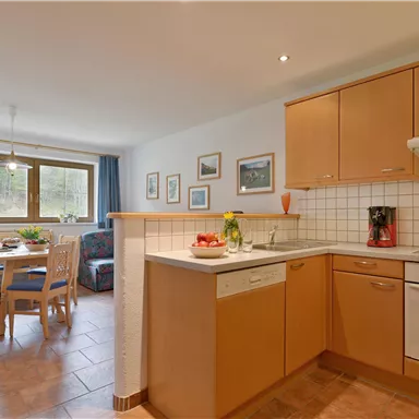 Eine moderne Küche mit Holzschränken und einem gemütlichen Essbereich. Viel Licht strömt durch die Fenster und schafft eine einladende Atmosphäre.