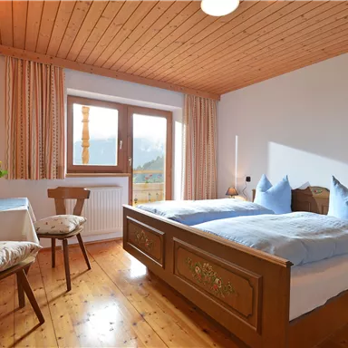 Ein gemütliches Schlafzimmer mit einem großen Bett und blauen Kissen. Ein Tisch und ein Stuhl ergänzen die helle, einladende Atmosphäre.