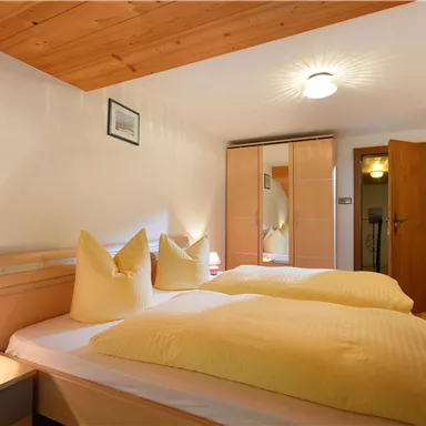 Ein gemütliches Schlafzimmer mit zwei Betten und gelben Kissen. Der Raum hat einen Holzdecken und einen großen Kleiderschrank.