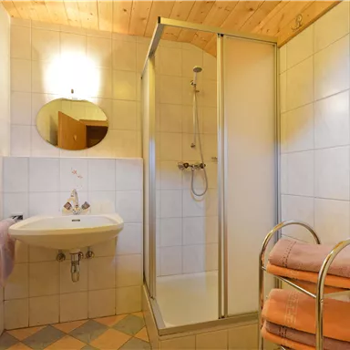 Ein modernes Badezimmer mit einer Dusche und einem Waschbecken. Handtücher sind ordentlich gestapelt auf einem Regal.