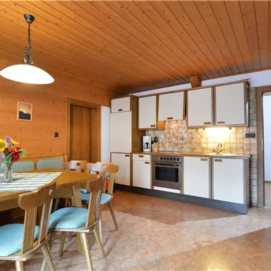 Eine gemütliche Küche mit einem Esstisch und Stühlen. Der Holzdecke und die hellen Schränke verleihen dem Raum eine warme Atmosphäre.