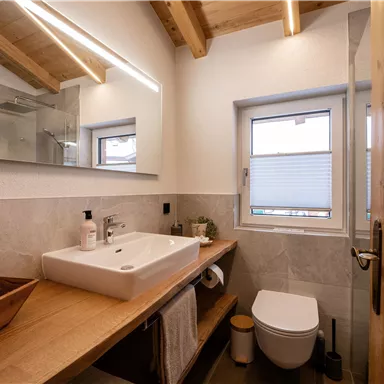 Ein modernes Badezimmer mit Holzdetails und einer eleganten Waschgelegenheit. Helle Wände und ein Fenster sorgen für ausreichend Tageslicht.