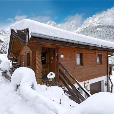 A cozy mountain chalet in the snow with a clear blue sky in the background. The snow surrounds the chalet and emphasizes the wintry mood.