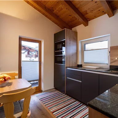 Eine moderne Küche mit Holzdecken und eleganten Möbeln. Am Tisch stehen frische Früchte und der Raum ist hell und einladend.