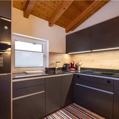 Eine moderne Küche mit Holzdecken und stilvollen schwarzen Möbeln. Die Ausstattung umfasst einen Backofen, eine Spüle und verschiedene Küchengeräte.