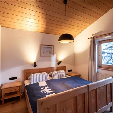 Ein gemütliches Schlafzimmer mit Holzwänden und einem Himmelbett. Große Fenster sorgen für viel Tageslicht und einen Blick nach draußen.