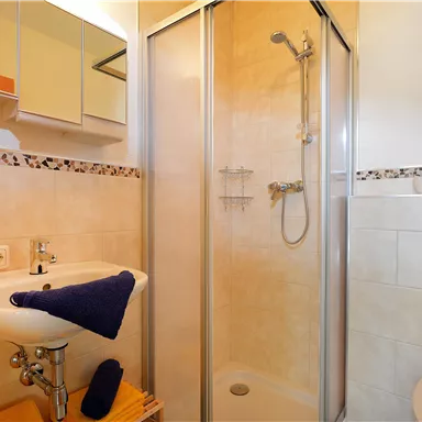 Ein modernes Badezimmer mit Dusche, Waschbecken und Spiegel. Die Wände sind hell gefliest und die Ausstattung ist funktional.