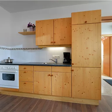 Eine helle Küche mit Holzschränken und einem modernen Herd. Der Raum hat eine gemütliche Atmosphäre und einen Zugang zu einem Flur.