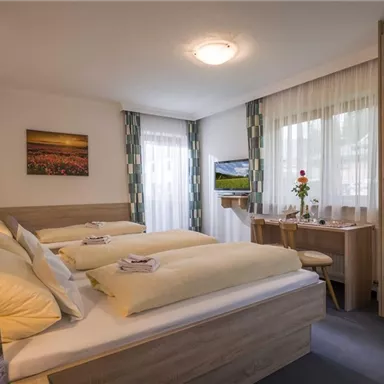 Ein gemütliches Schlafzimmer mit zwei Betten, sanften Farben und viel natürlichem Licht. Der Raum ist modern eingerichtet und bietet einen Schreibtisch sowie einen Fernseher.